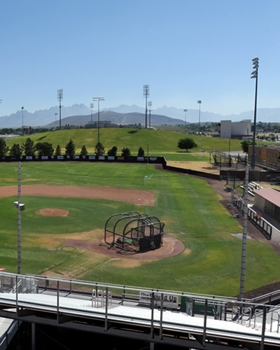 A sunny aerial view of green grass on the Presley Askew Field. The Organ mountains and A mountain draping the desert background.