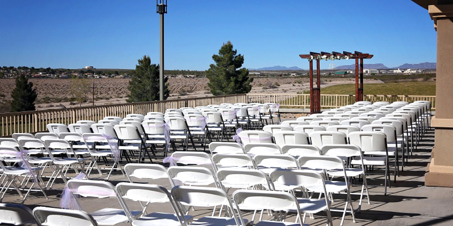 Outdoor wedding ceremony setup with rows of white chairs facing a scenic desert backdrop.