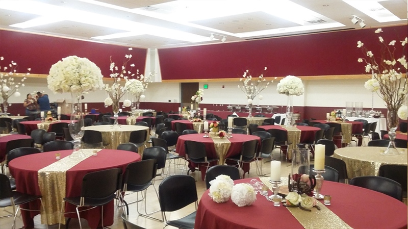 Ballroom filled with round tables decorated with red and gold table cloths adorned with vertical floral centerpieces.