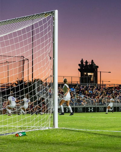 The women's soccer team on the soccer field with a vibrant sunset in the background, showcasing an exciting moment in the game.